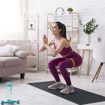stay home strength training beautiful girl doing squats with rubber band in light room empty space