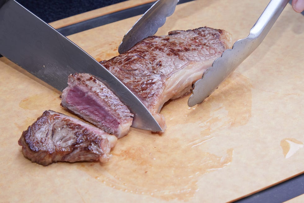 sliced steak on a cutting board with tongs and knife