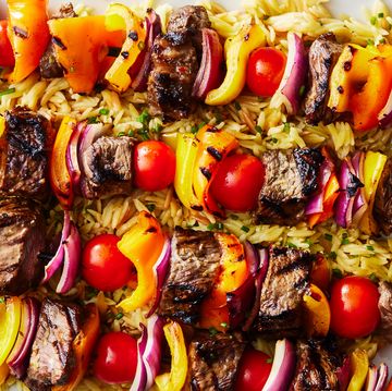steak kebabs with peppers on top of orzo with a spinach cucumber salad