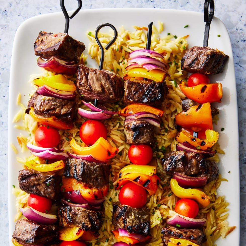 steak kebabs with peppers on top of orzo with a spinach cucumber salad