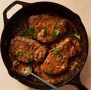 three steaks in a brown cream sauce garnished with parsley in a cast iron pan with a spoon sticking out of it