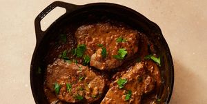 three steaks in a brown cream sauce garnished with parsley in a cast iron pan with a spoon sticking out of it