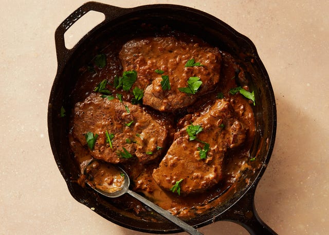 three beef tenderloin steaks covered in creamy brown sauce and chopped parsley in a cast iron pan with a spoon sticking out of it three beef tenderloin steaks covered in creamy brown sauce and chopped parsley in a cast iron pan with a spoon sticking out of it