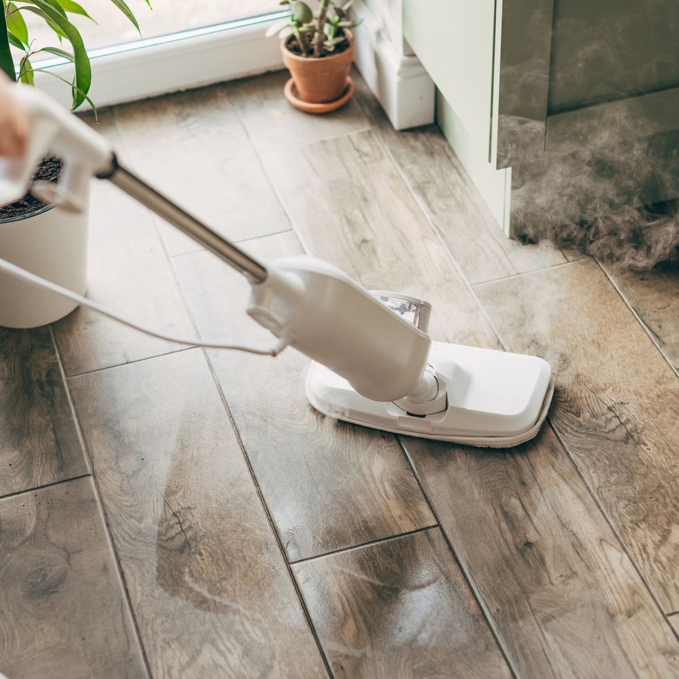 woman cleaning floor with steam mop in kitchen at home, closeup