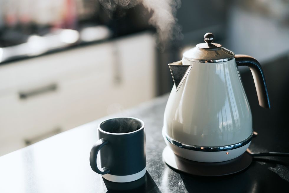 steam coming out from a kettle over the kitchen counter, with a cup by the side
