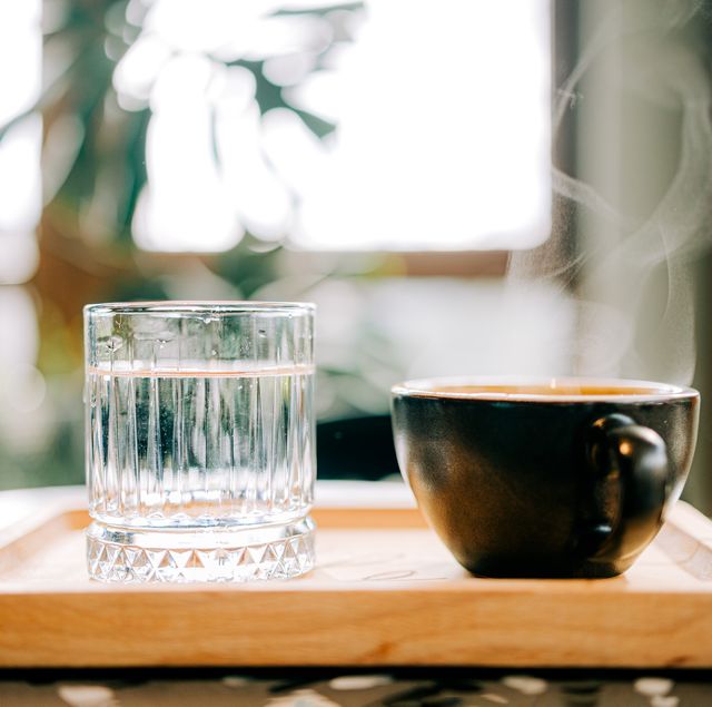 steaming cup of coffee and glass of water on wooden tray