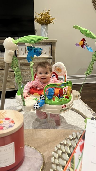 a baby in a fisherprice jumperoo, white and green baby toy with a baby girl sitting inside, part of good housekeepings test of the best baby jumpers