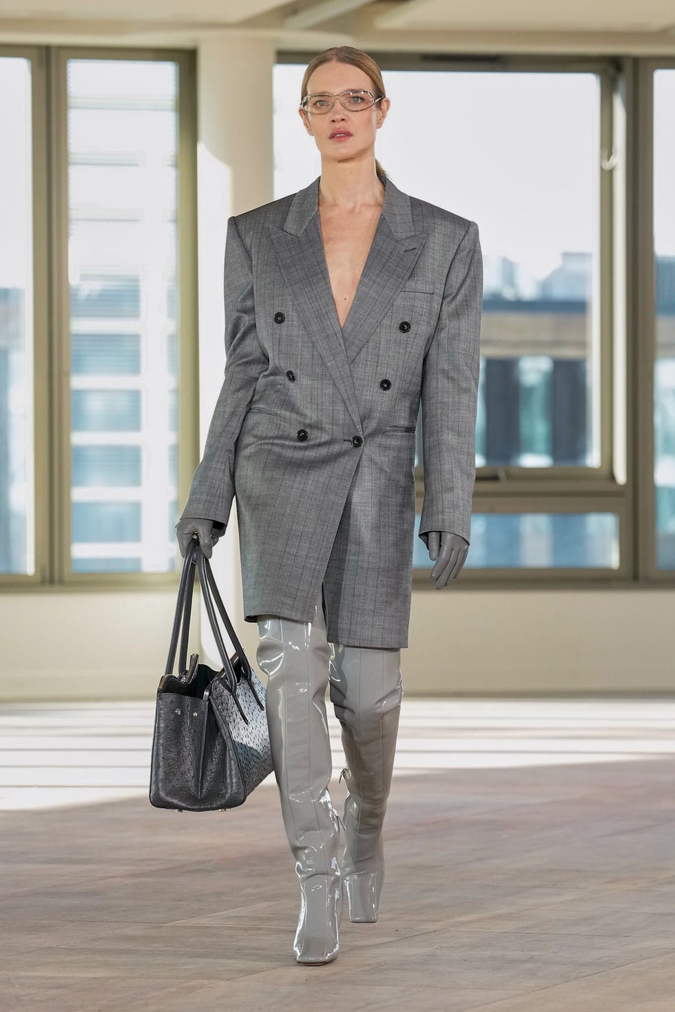 fashion model showcasing a contemporary outfit featuring a tailored gray blazer and glossy thighhigh boots