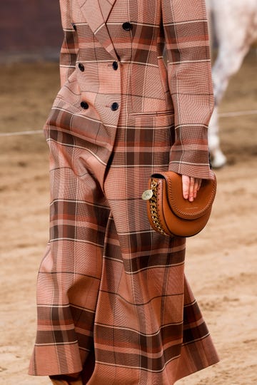 a model walking in a fashion show wearing a tailored plaid suit and holding a handbag