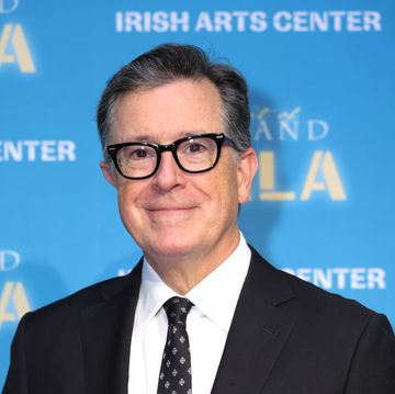 stephen colbert smiling for a red carpet photo in a black suit and patterned black tie