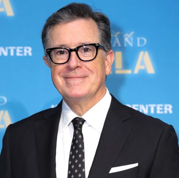 stephen colbert smiling for a red carpet photo in a black suit and patterned black tie