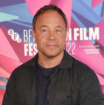 stephen graham stands clasping hands and looking at the camera, he wears black trousers, tshirt, jacket and trainers