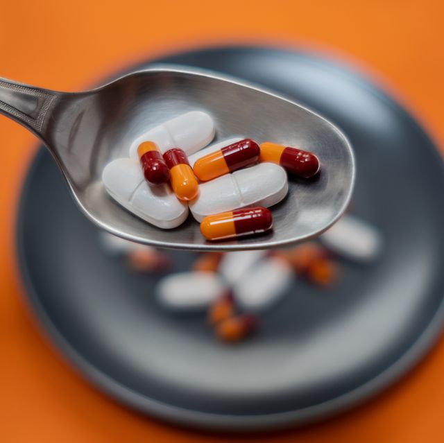 foreground focus on a spoon full of pills and capsules soft focus on the background plate full of capsules and pills