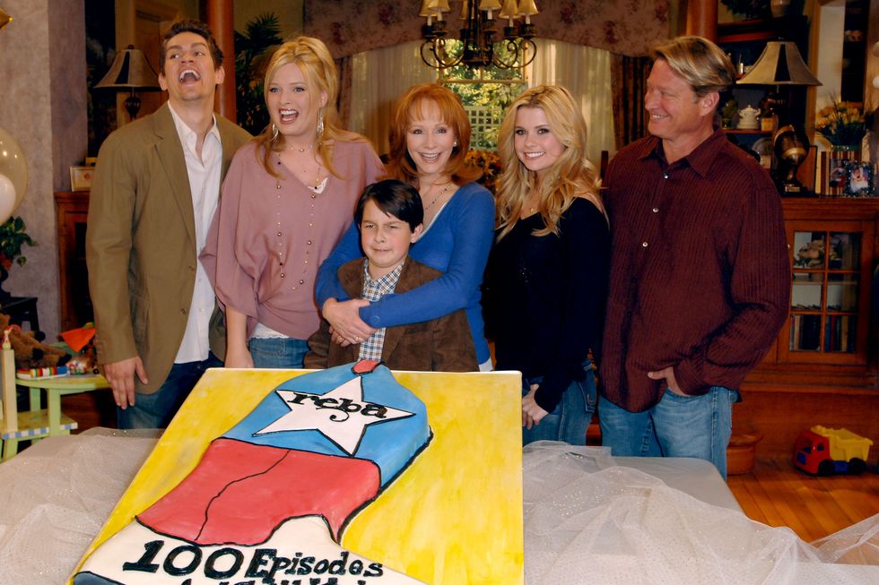 reba cast members cutting into a large cake in celebration of 100 episodes