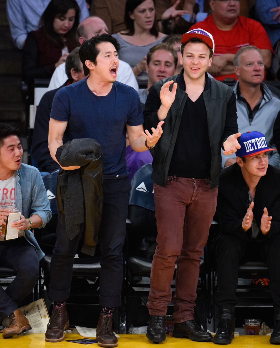 steven yeun holding a jacket and cheering courtside at an nba game