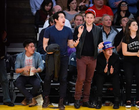 steven yeun holding a jacket and cheering courtside at an nba game