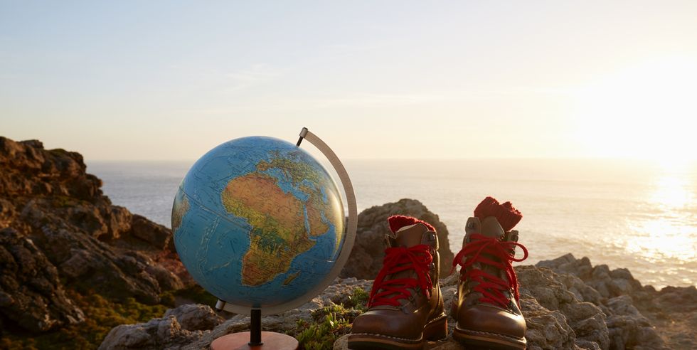 still life of globe and hiking boots on cliff by sea