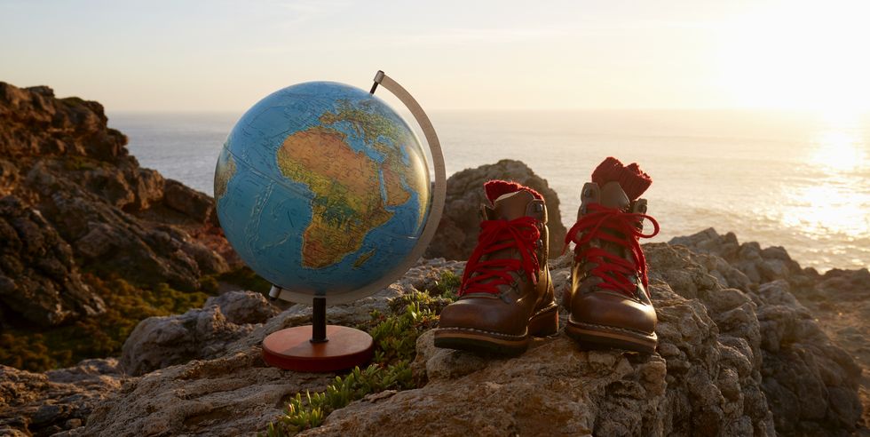 still life of globe and hiking boots on cliff by sea