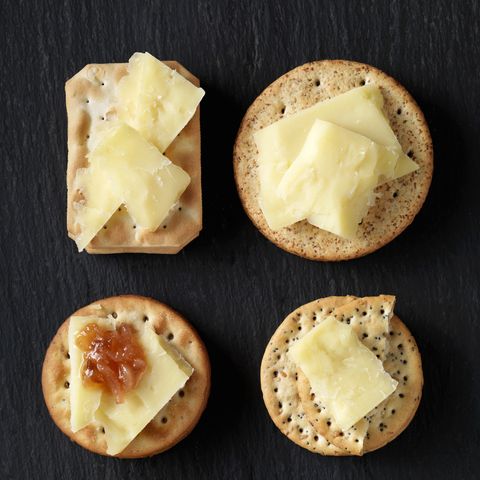 still life of variety of cheese crackers with cheddar cheese and chutney on black slate, overhead view