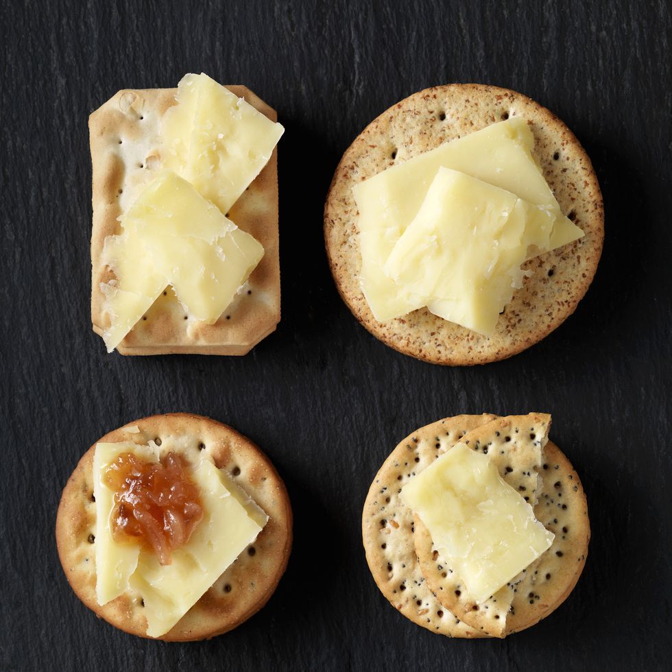 still life of variety of cheese crackers with cheddar cheese and chutney on black slate, overhead view
