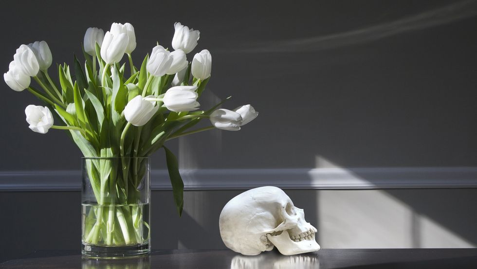 still life picture showing flowers and human skull on the table