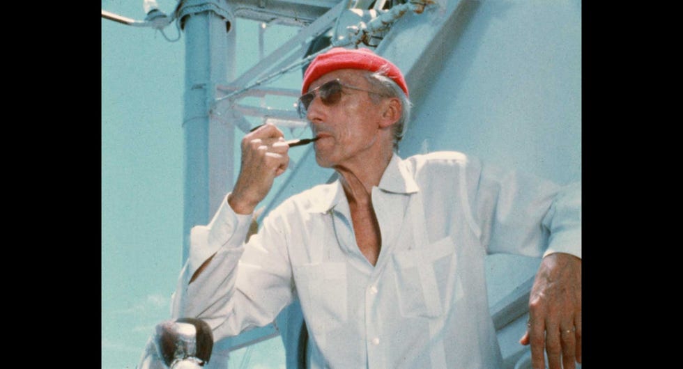 Cousteau met zijn herkenbare rode scheepsmuts op aan boord van de Calypso een afgedankte mijnenveger die hij verbouwde tot onderzoeksschip