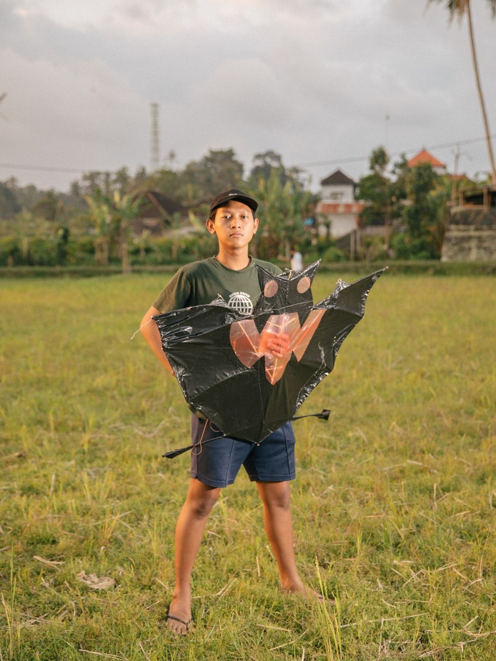 Komang Windu poseert voor een portret met zijn vlieger in een rijstveld bij het dorp Tunjuk