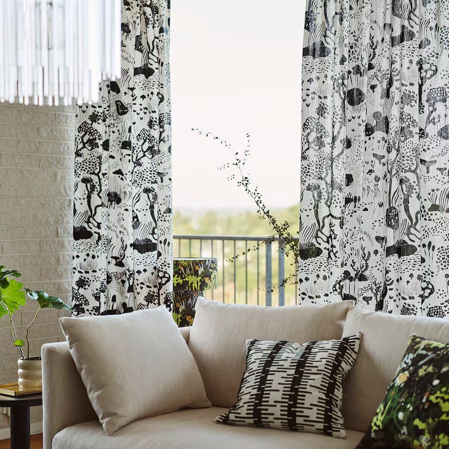 living room featuring patterned curtains a neutral sofa and decorative pillows