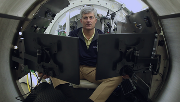 man sitting in a submersible with computers all around him