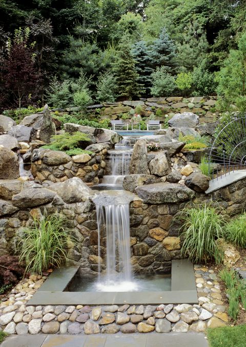 stone waterfall in a yard with pine trees