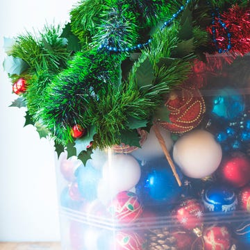 storage of christmas decorations christmas balls, decorations, tinsel and garlands in a large plastic box on a wooden table, light background