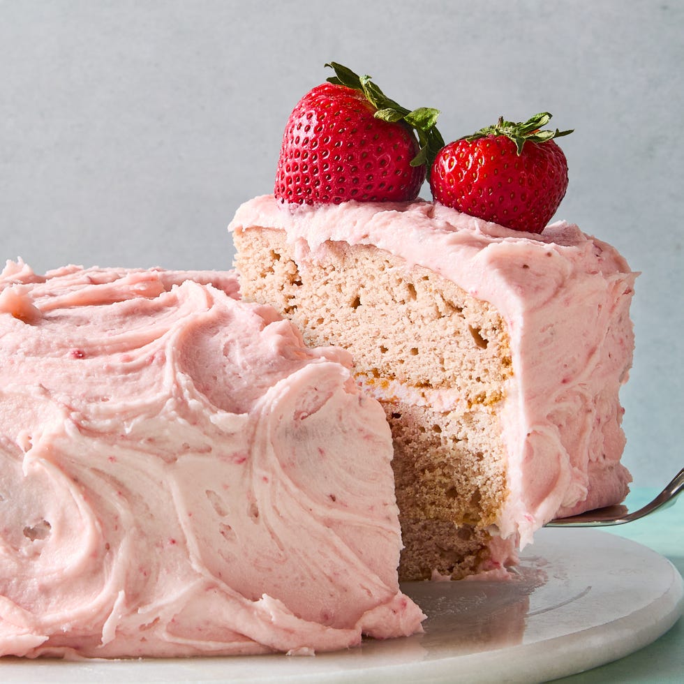layered strawberry cake with pink icing and a strawberry on top