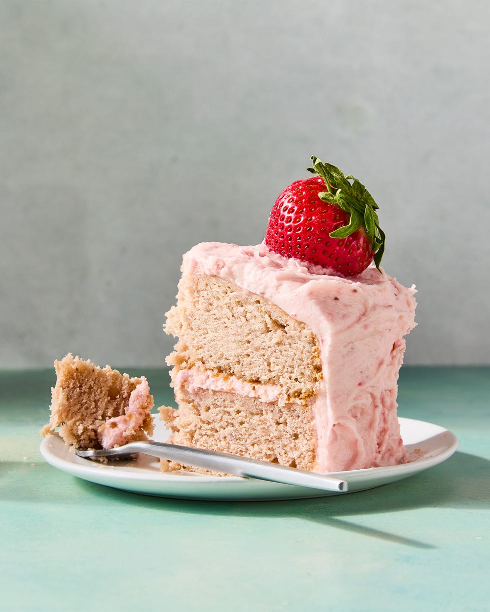 layered strawberry cake with pink icing and a strawberry on top