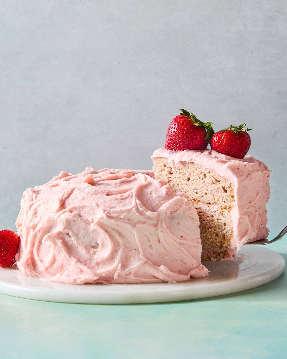 layered strawberry cake with pink icing and a strawberry on top