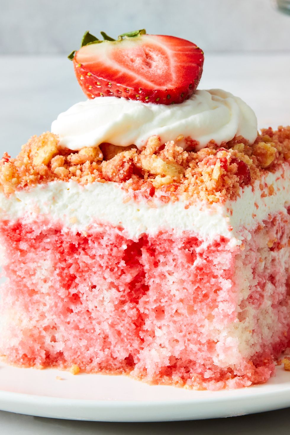 strawberry crunch poke cake with a crumble topping, whipped cream and strawberries