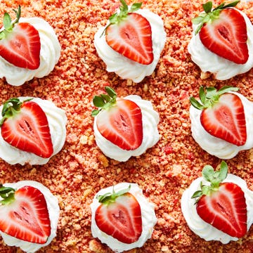 strawberry crunch poke cake with a crumble topping, whipped cream and strawberries