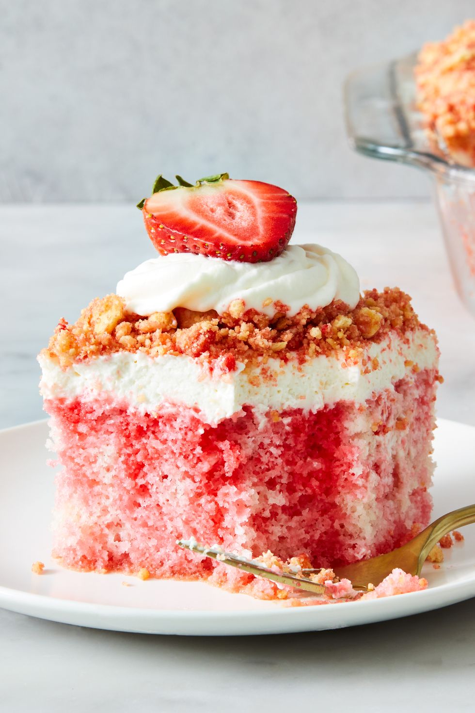 strawberry crunch poke cake with a crumble topping, whipped cream and strawberries