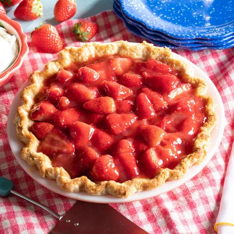 strawberry pie on gingham napkin with whipped cream, forks, and blue plates