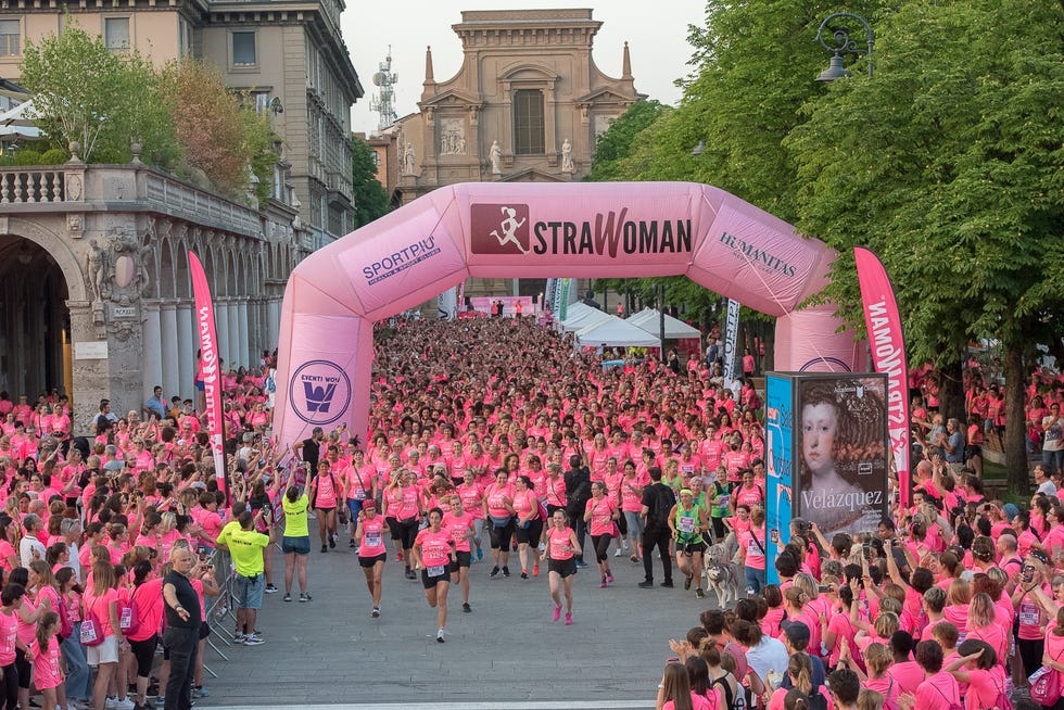 Crowd of participants running under a large inflatable archway with the text STRAWoman during a race event