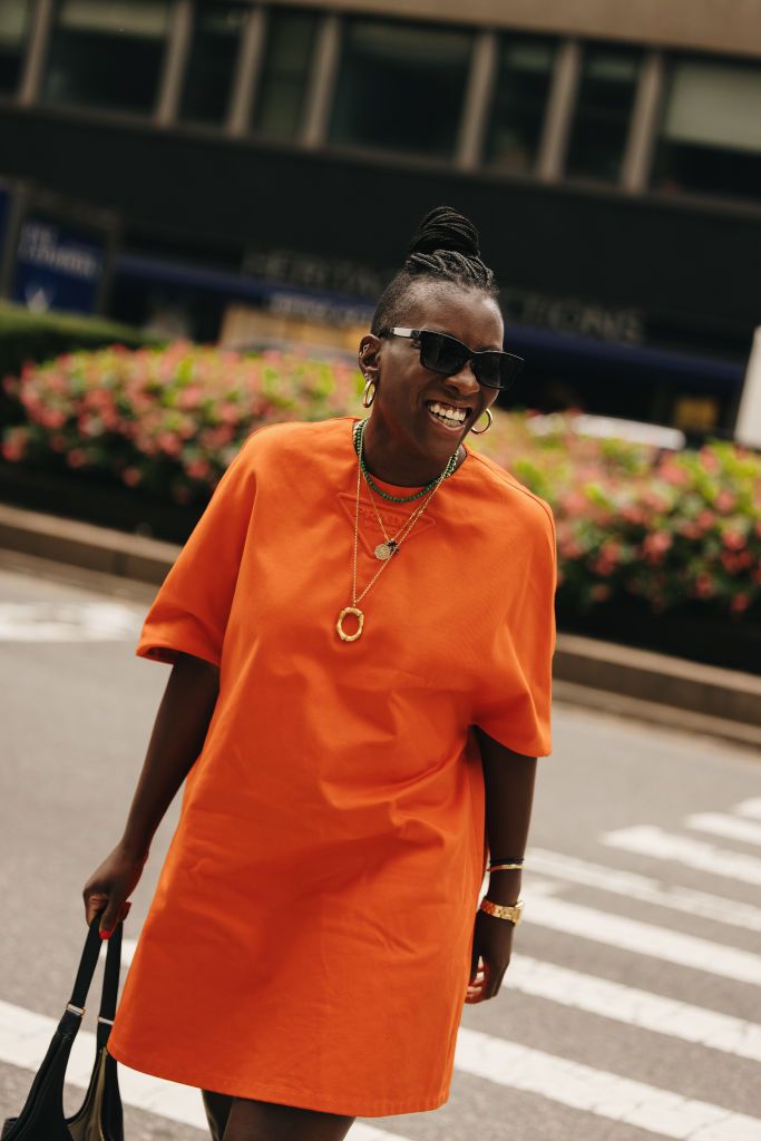 nikki ogunnaike wearing an orange shirt dress, necklaces, bracelets, and carrying a leather bag in a roundup of the best travel outfits for women 2024