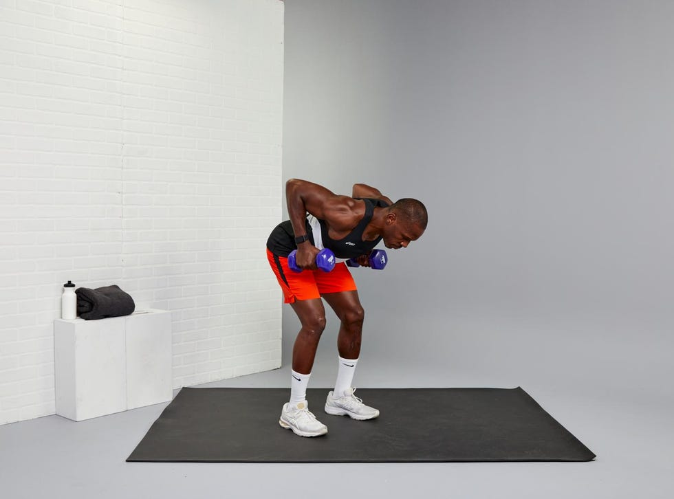 man performing a dumbbell exercise on a mat in a gym setting