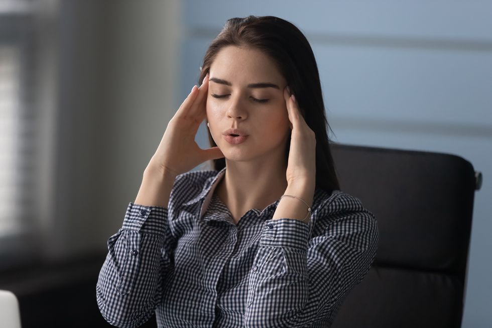 stressed woman massaging temples, trying control work pressure at office