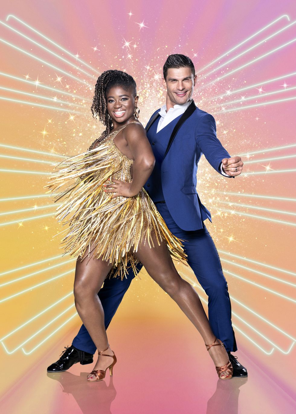 strictly come dancing 2020 couples   clara amfo, in a gold sequinned dress, and aljaz skorjanec, in a blue suit, standing against a pink and orange background