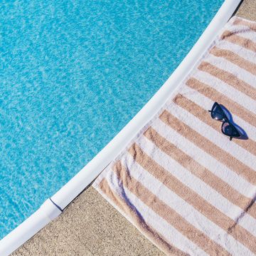 summer background striped beach towel with cateye sunglasses next to swimming pool