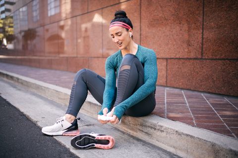 Strong athletic woman massaging her foot to get rid of a foot cramp while sitting on a sidewalk