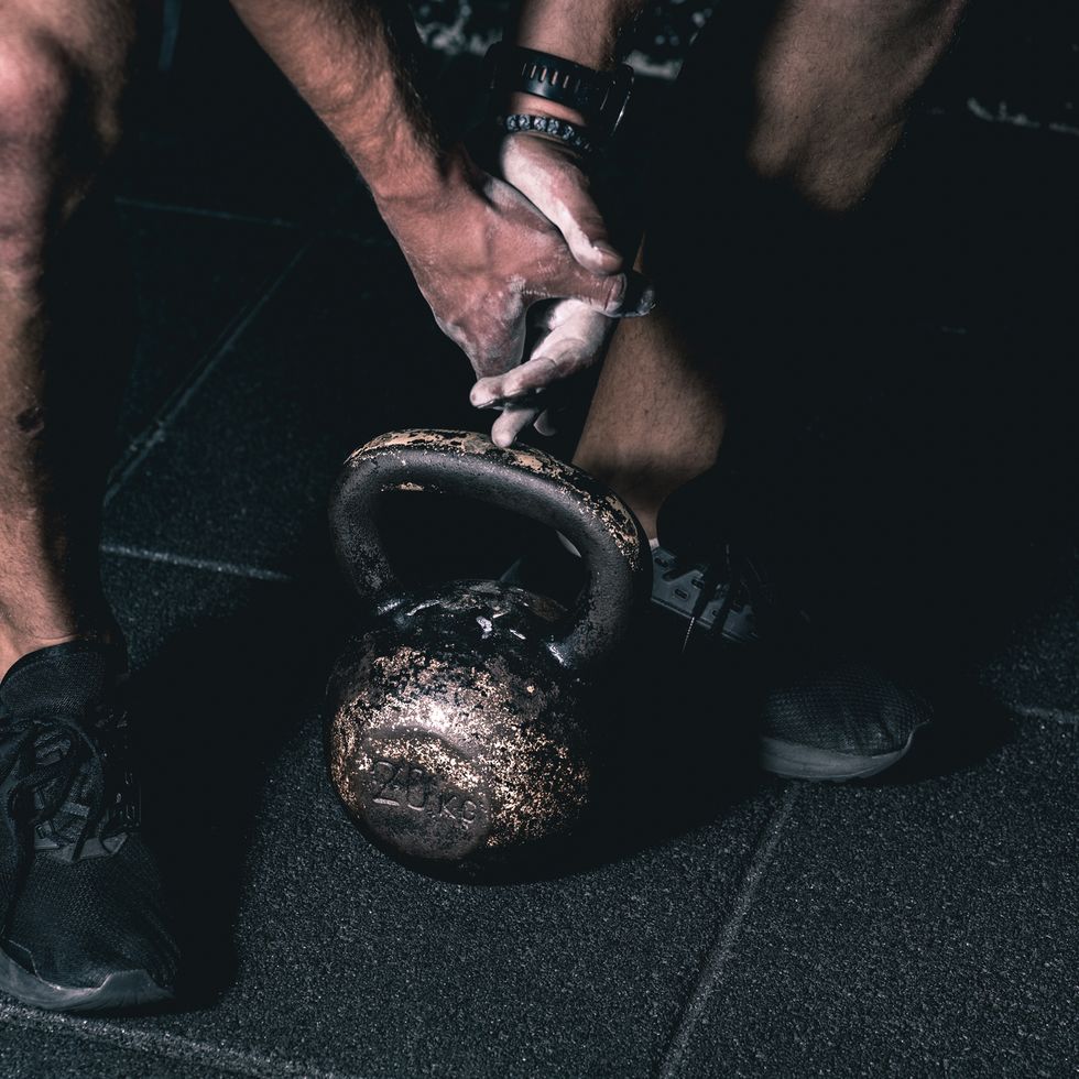 Strong muscular man with muscles holding heavy red kettlebell with his hand on the gym floor prepared for cross strength and conditioning training and workout