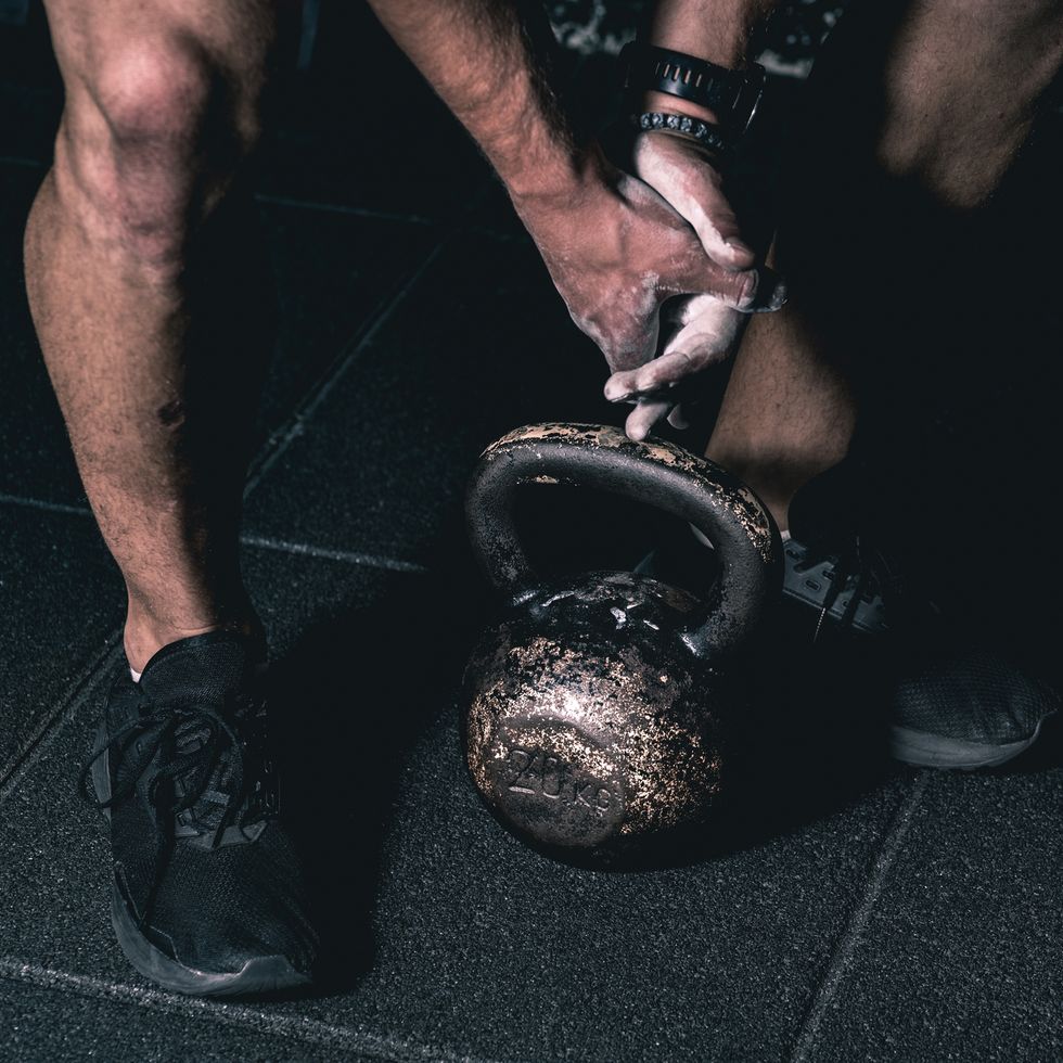 Strong muscular man with muscles holding heavy red kettlebell with his hand on the gym floor prepared for cross strength and conditioning training and workout