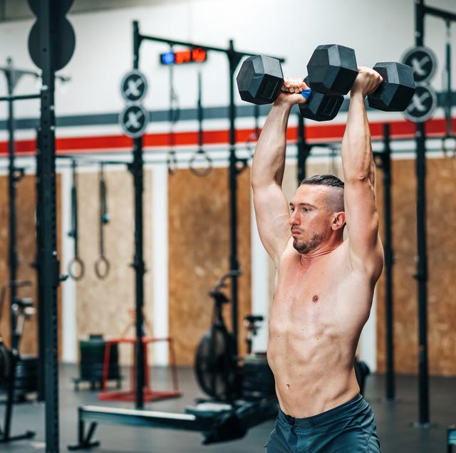 strong sportsman doing dumbbells exercise in gym with equipment