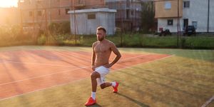 Strong sporty man stretching his legs before training. Standing in tennis playground on hot summer morning.