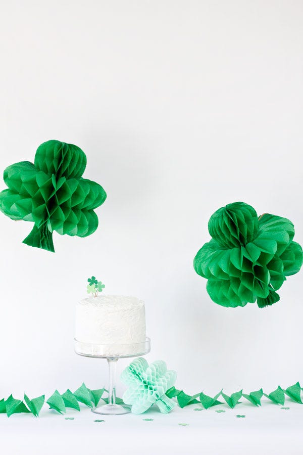 Two green paper honeycomb shamrocks hanging on top of a white cake decorated with a green clover topper